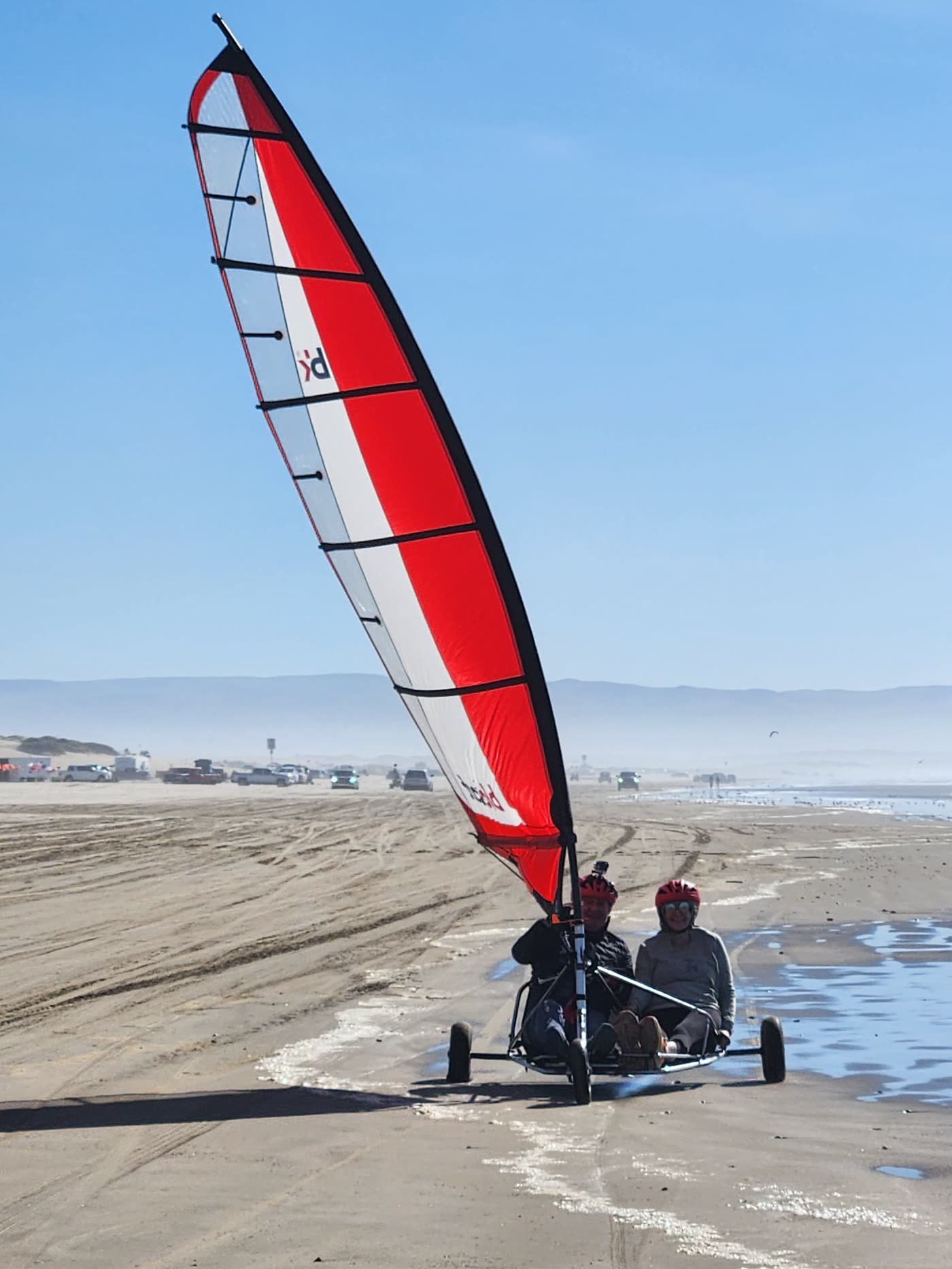 Two riders in a red-and-white sail kart on the wide beach at Pismo